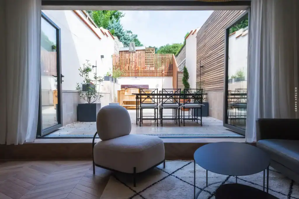 Jolie cour intérieure avec mobilier moderne et végétation, vue depuis salon lumineux.