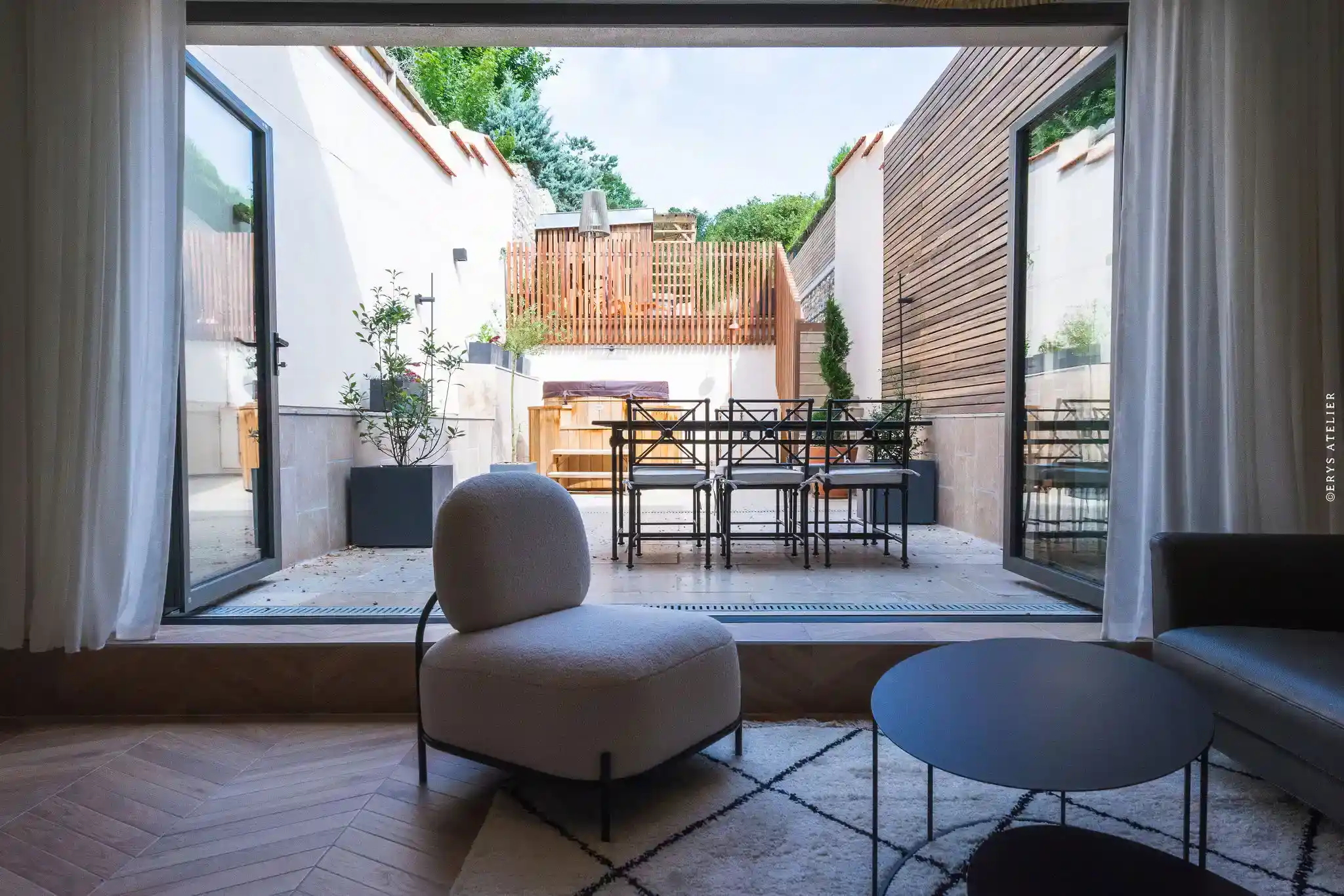 Jolie cour intérieure avec mobilier moderne et végétation, vue depuis salon lumineux.
