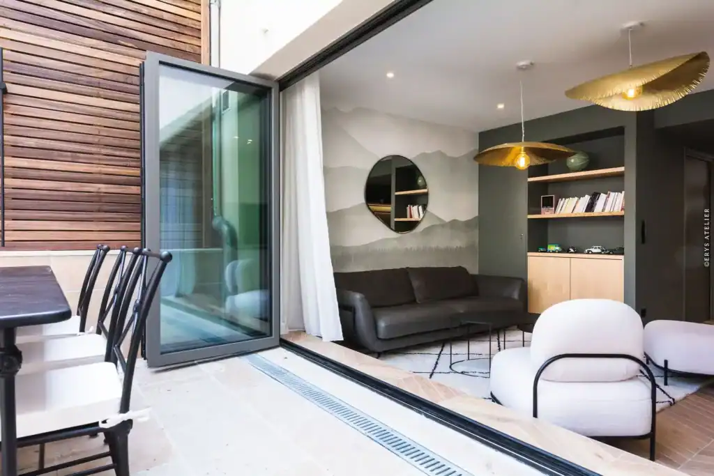 Bureau ouvert avec grande baie vitrée donnant sur une terrasse en bois, intérieur moderne et lumineux avec meubles élégants.