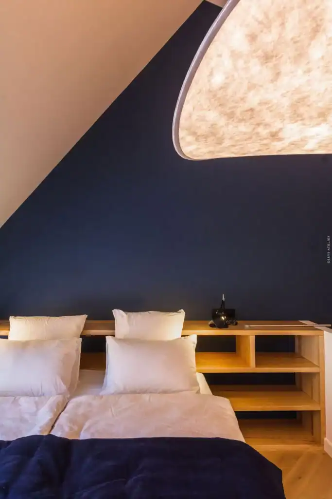 Chambre contemporaine avec éclairage élégant, murs bleus profonds et mobilier en bois naturel.