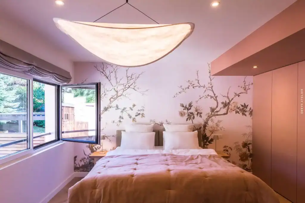 Lit dans une chambre élégante avec mur peint de branches florales, lumière naturelle et décoration moderne.