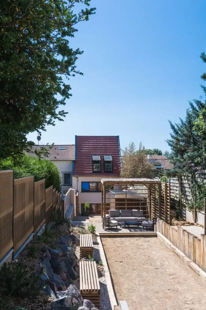 Salon de jardin sous pergola en bois et canisses, terrin de pétanque, bancs en bois
