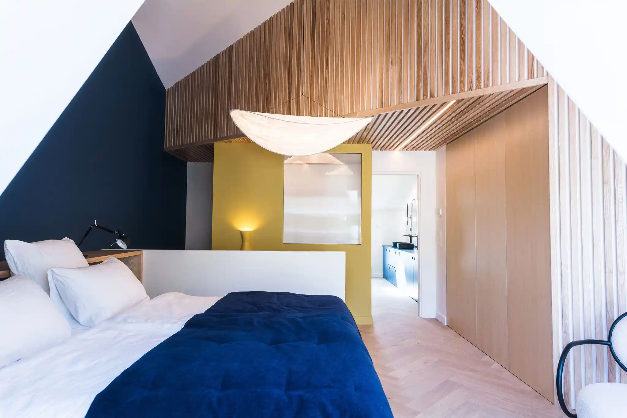 Lit moderne avec décoration épurée, mur bleu foncé et lampe suspendue en tissu blanc.