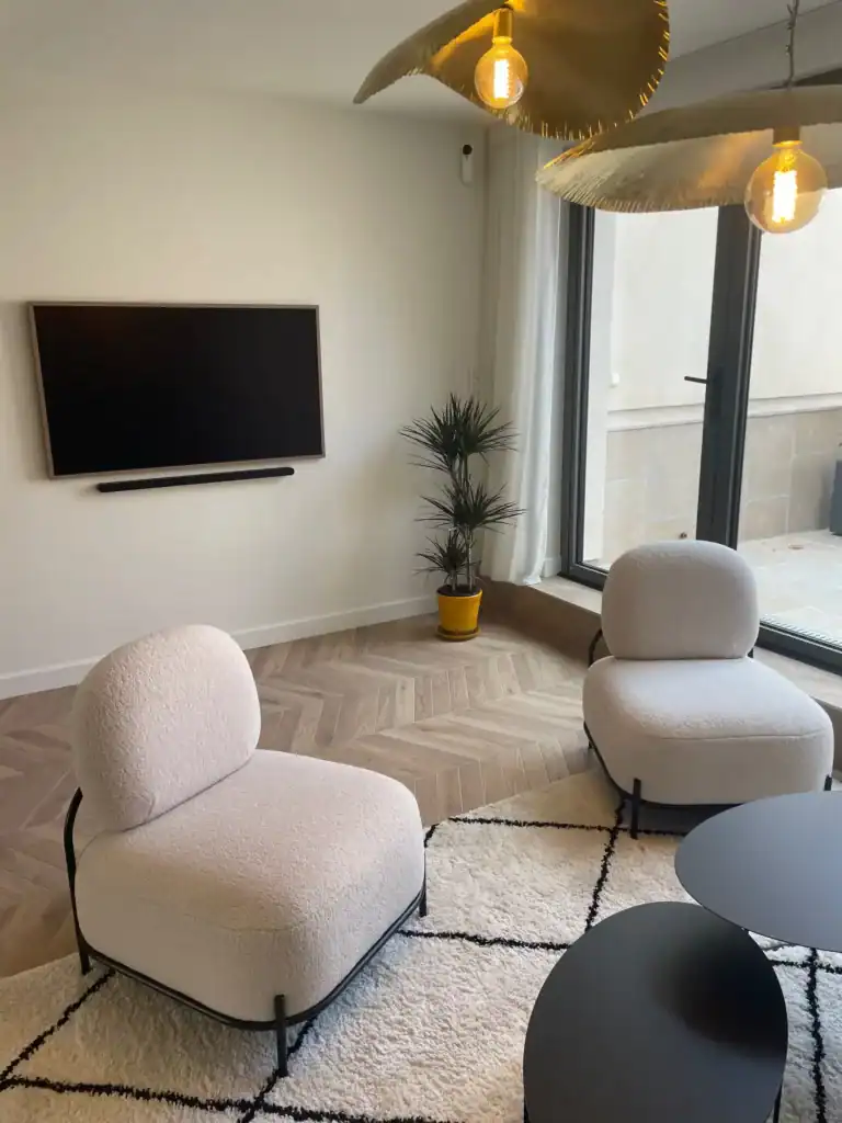 Salle de séjour moderne avec fauteuils blancs, télévision murale et terrasse lumineuse.