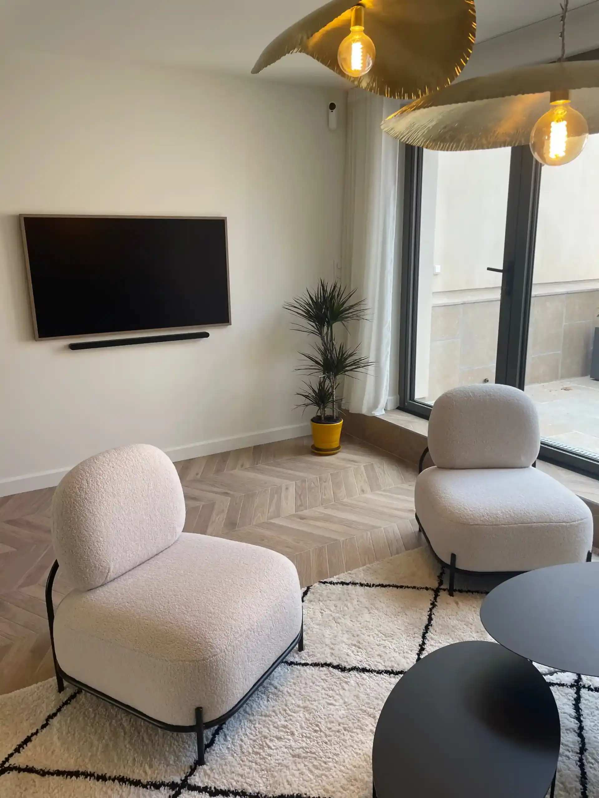 Salle de séjour moderne avec fauteuils blancs, télévision murale et terrasse lumineuse.